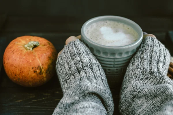 Woman Hands with Spicy pumpkin latte on a wooden board with a sw