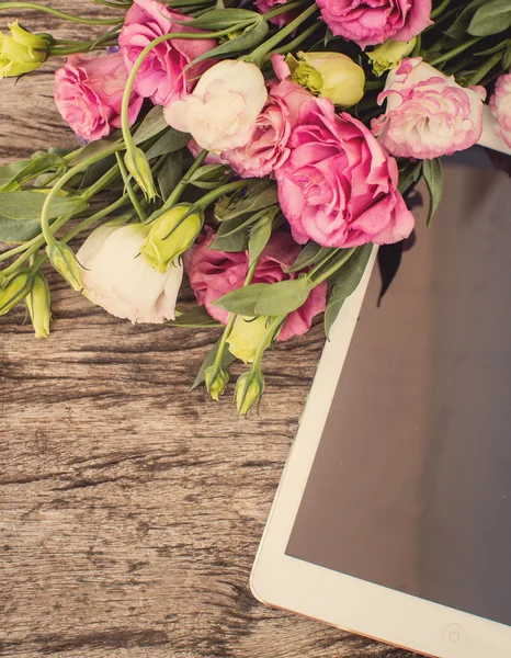 Bouquet of flowers on a  wooden table with a tablet computer wit