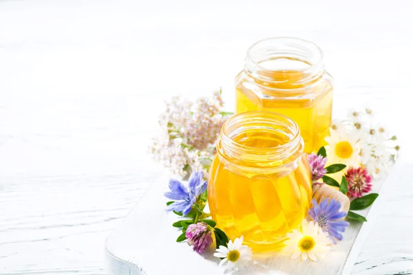 Jars with fresh flower honey on white board