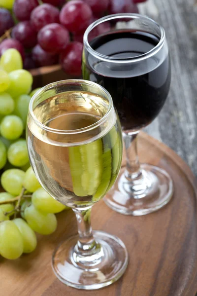 Glasses of white and red wine, fresh grapes on a wooden board
