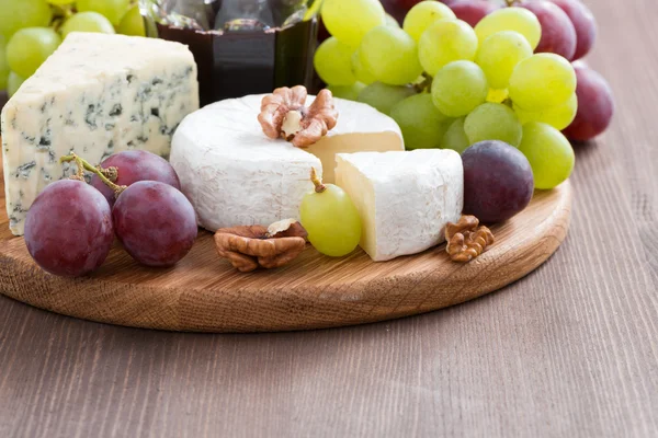 Assorted soft cheeses and fresh grapes on a wooden background