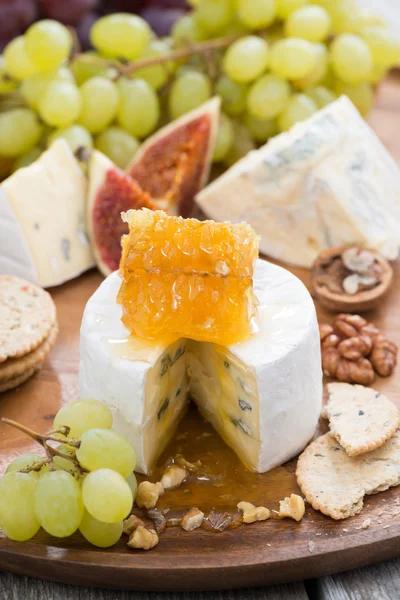 Camembert with honey and fruit close-up on a wooden tray, vertic