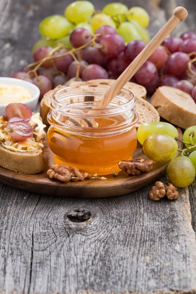 Flavored honey, bread and butter and grapes on a wooden backgrou