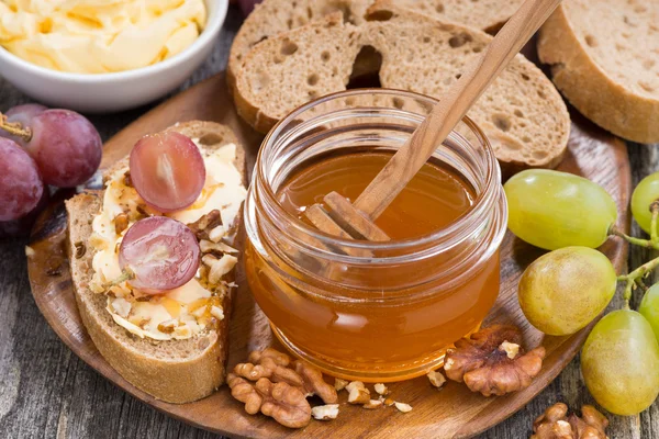 Flavored honey, bread with butter and grape on wooden board, top