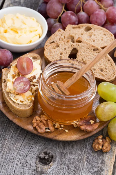 Flavored honey, bread with butter and grape on wooden board
