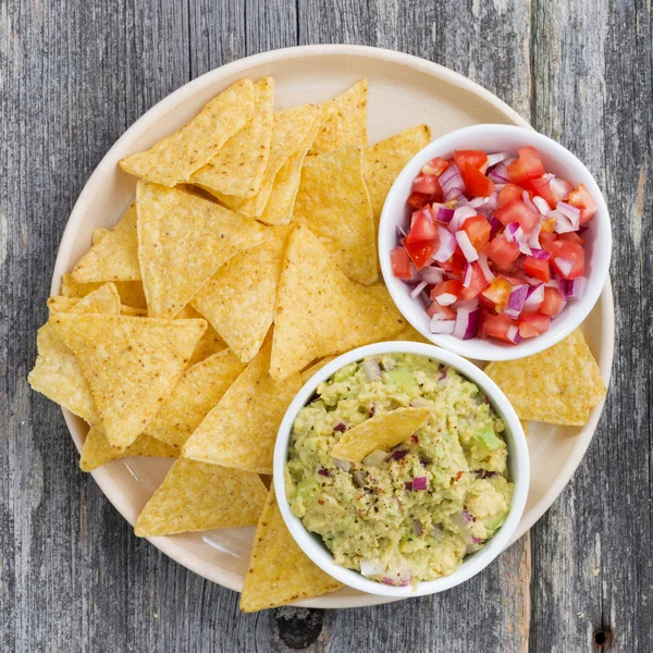 Guacamole, tomato salsa and corn chips on a plate, top view