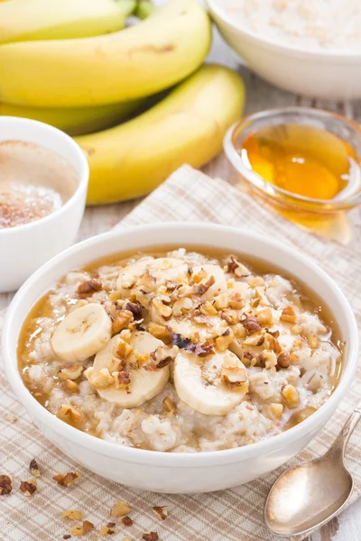 Oatmeal with banana, honey and walnuts in bowl for breakfast