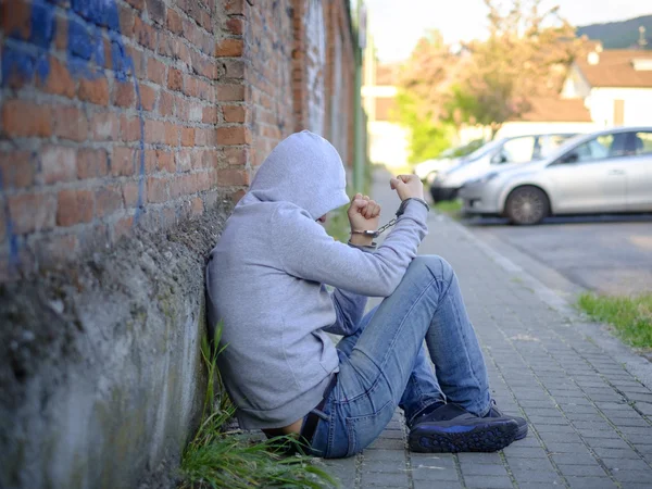 Portrait of handcuffed man with face hidden by sweatshirt hood