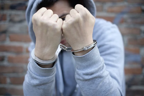 Portrait of handcuffed man with face hidden by sweatshirt hood