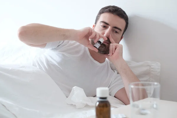 Man feeling cold and using a nasal spray lying in the bed