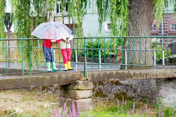 Two little kid boys with big umbrella outdoors