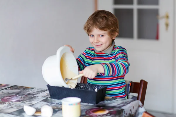 Funny blond kid boy baking cake indoors