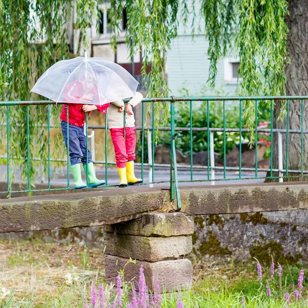 Two little kid boys with big umbrella outdoors