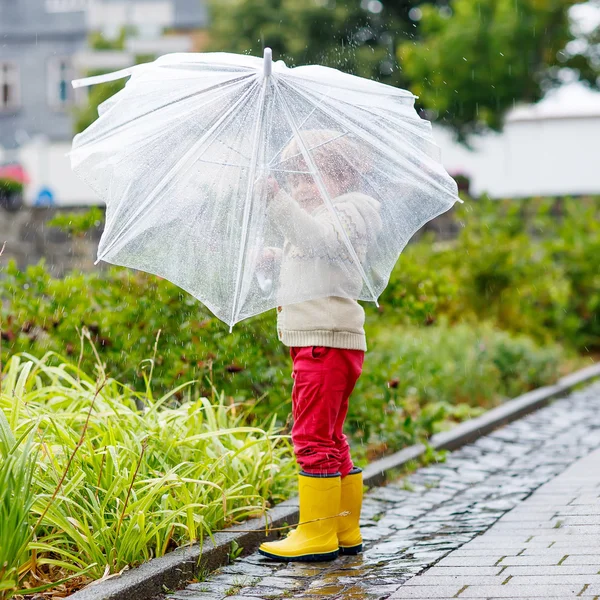 Little blond kid boy walking with big umbrella outdoors