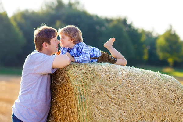 Father and little son having fun on yellow hay field in summer