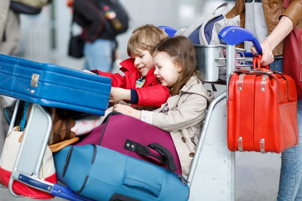 Little girl and boy sitting on suitcases on airport