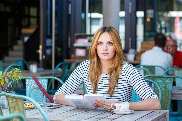 Woman drinking coffee and reading book in cafe