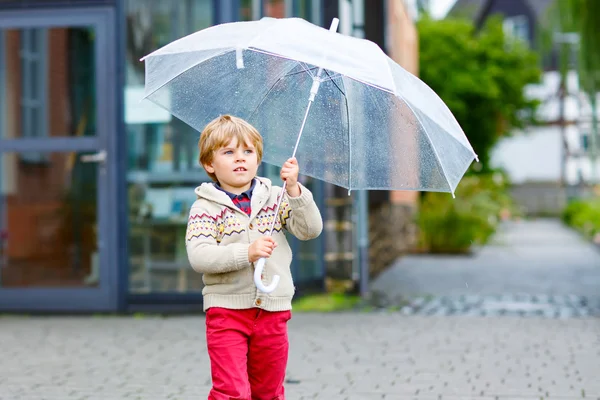 Little blond kid boy walking with big umbrella outdoors