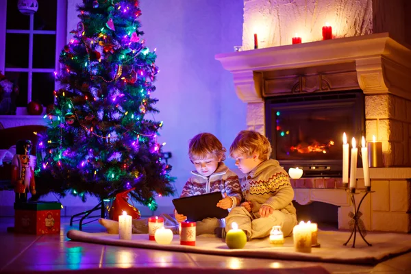 Two little children sitting by a fireplace at home at Christmas