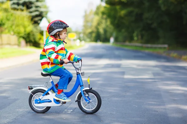 Adorable kid boy in red helmet and colorful raincoat riding his