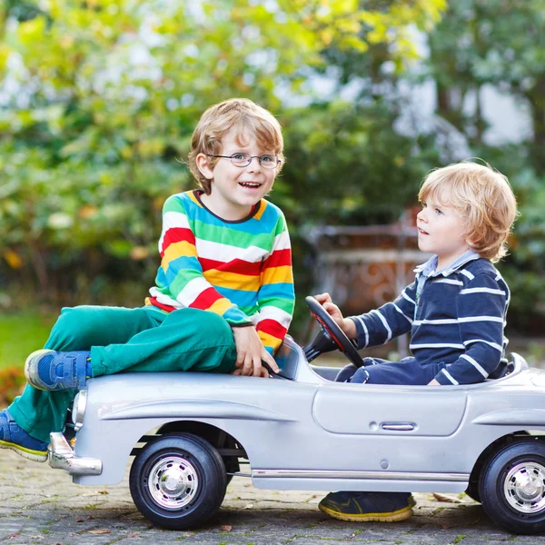 Two happy kids playing with big old toy car in s