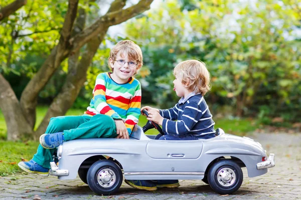 Two happy kids playing with big old toy car in summer garden, ou