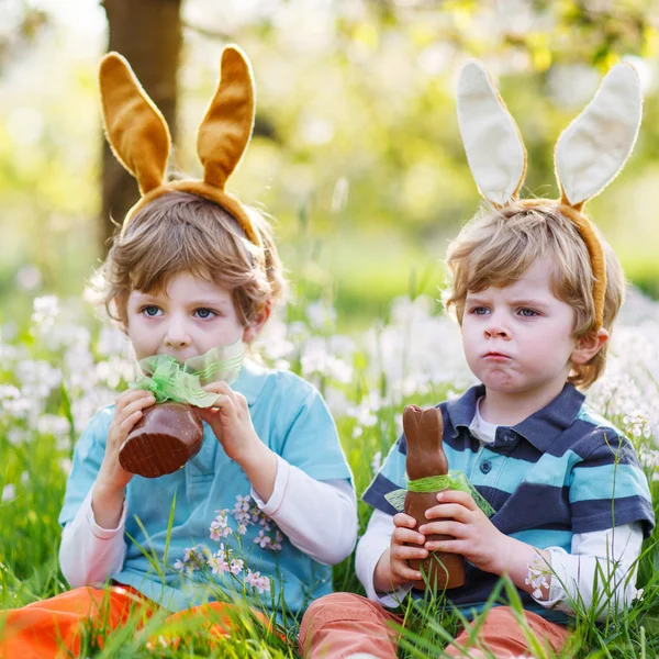 Two little boys wearing Easter bunny ears and eating chocolate