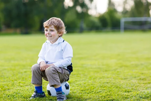 Blond boy of 4 resting with football on football field