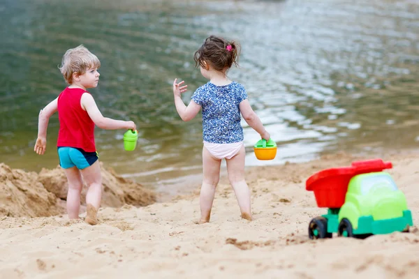 Little toddler boy and girl playing together with sand toys near