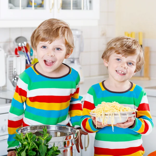 Two little kid boys eating spaghetti in domestic kitchen.