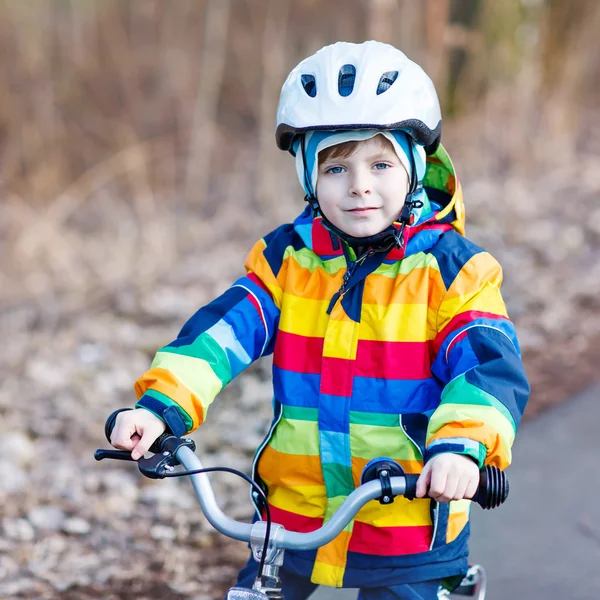 Kid boy in safety helmet and colorful raincoat riding bike, outd