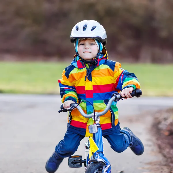 Funny cute  preschool kid boy in safety helmet and colorful raincoat riding his first bike