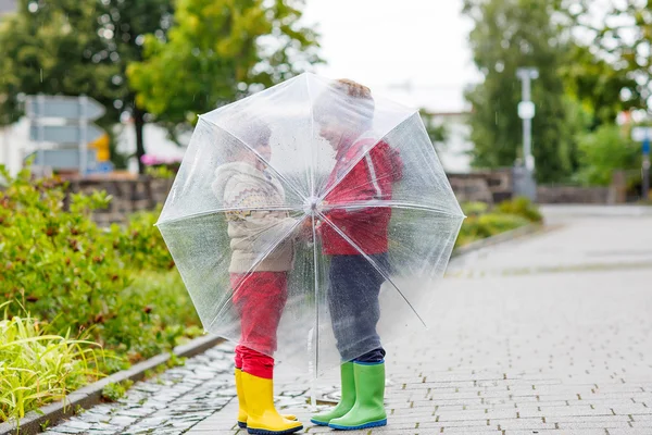 Two little kid boys with big umbrella outdoors