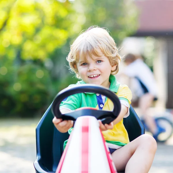 Little kid boy driving pedal car in summer garden