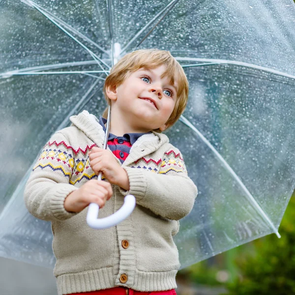 Little blond kid boy walking with big umbrella outdoors