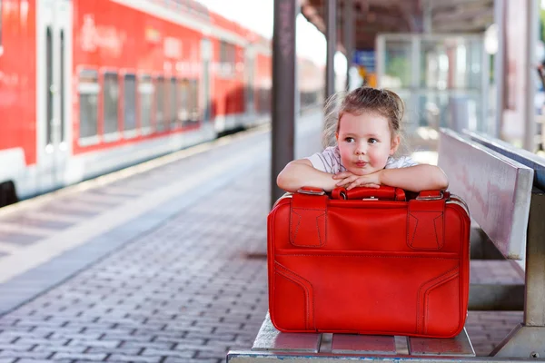 Little girl with big red suitcase on a railway station