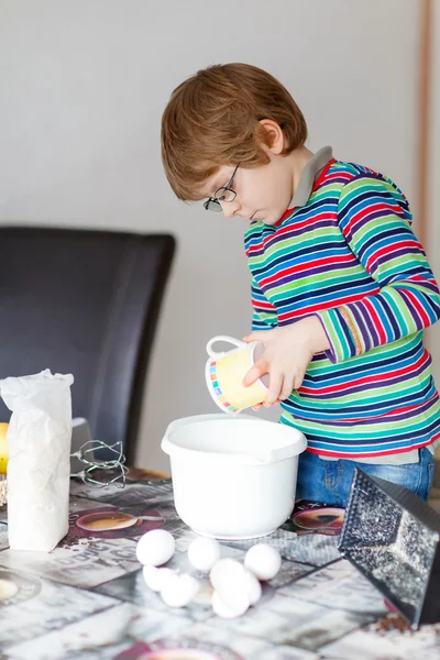 Funny blond kid boy baking cake indoors