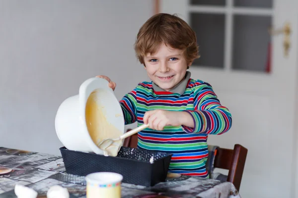 Funny blond kid boy baking cake indoors