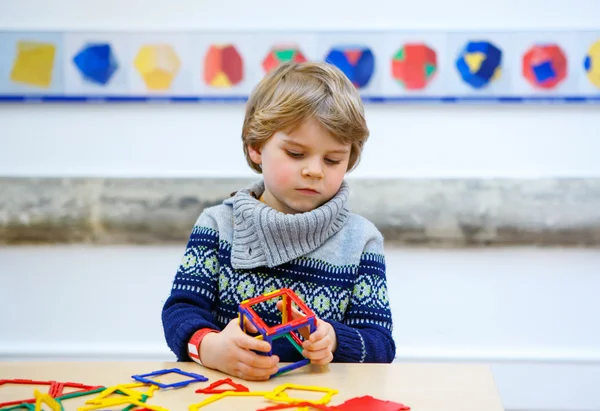 Little kid boy building geometric figures with plastic blocks