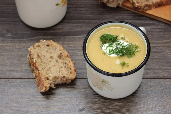 Lentil cream soup with cream cheese and dill in mug over rustic wooden background