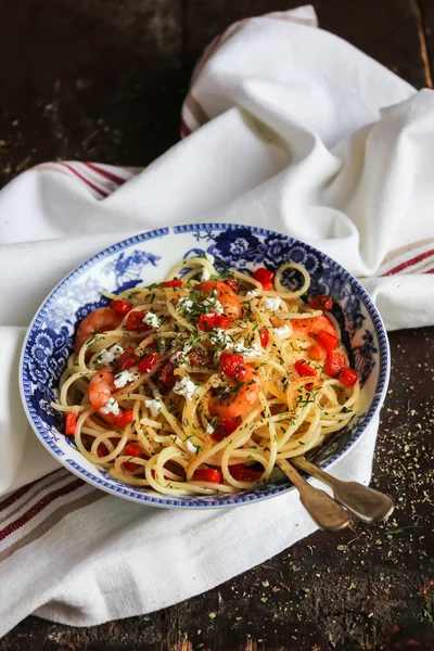 Cooked spaghetti pasta dish with roasted shrimps, chopped fresh tomatoes, red sweet pepper and salted greek feta cheese with chopped fresh dill in a bowl