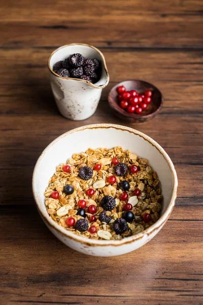 Healthy breakfast with homemade muesli or granola from baked oat flakes, fresh blackberry, red and black currant, toasted peanuts in a bowl