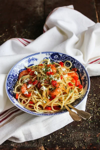 Cooked spaghetti pasta dish with roasted shrimps, chopped fresh tomatoes, red sweet pepper and salted greek feta cheese with chopped fresh dill in a bowl