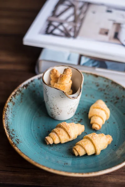 Homemade freshly baked short crust pastry crescent rolls cookies with sugar on a plate on a wooden rustic dark brown table, selective focus