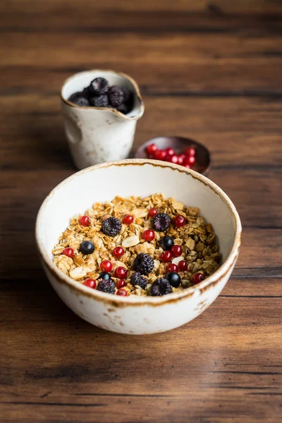 Homemade granola or muesli with oat flakes, corn flakes, dried fruits and toasted peanuts with fresh berries in a bowl, selective focus