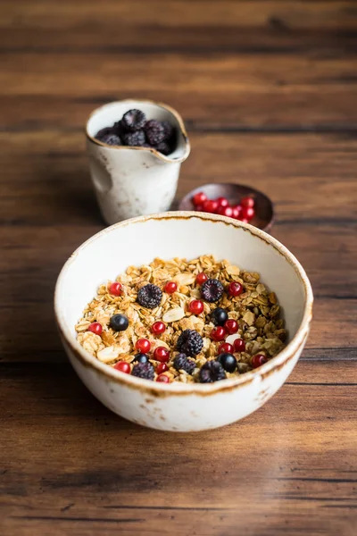 Homemade granola or muesli with oat flakes, corn flakes, dried fruits and toasted peanuts with fresh berries in a bowl, selective focus