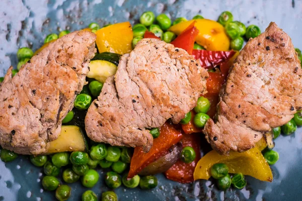 Roasted pork meat fillet chops with zucchini, onion, yellow and orange bell pepper, frozen peas on a plate with cream sauce, selective focus