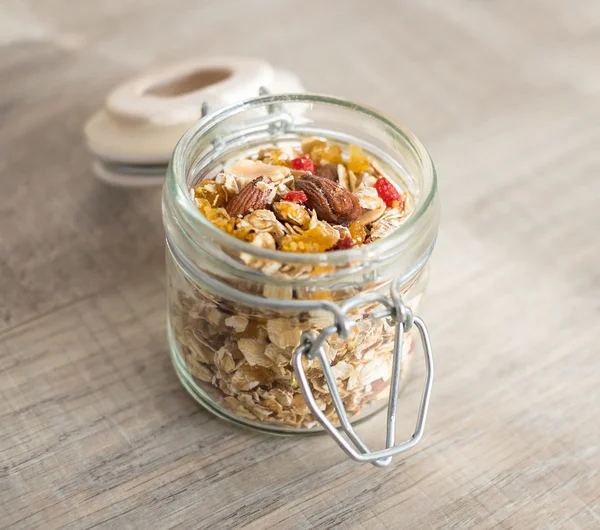 Homemade organic granola or muesli with goji berries, almond nuts, peanuts, oat flakes, honey in a jar on a wooden table, selective focus