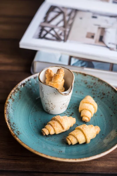 Homemade freshly baked short crust pastry crescent rolls cookies with sugar on a plate on a wooden rustic dark brown table, selective focus