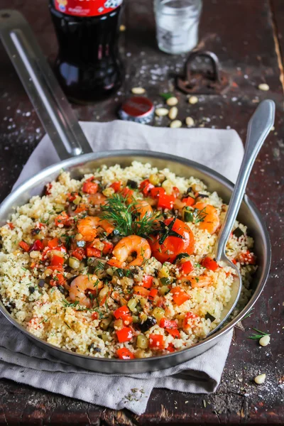 Homemade couscous with eggplant, zucchini, red pepper, cherry tomatoes, pine nuts and fresh dill in a pan ready for lunch or dinner on a wooden table, selective focus